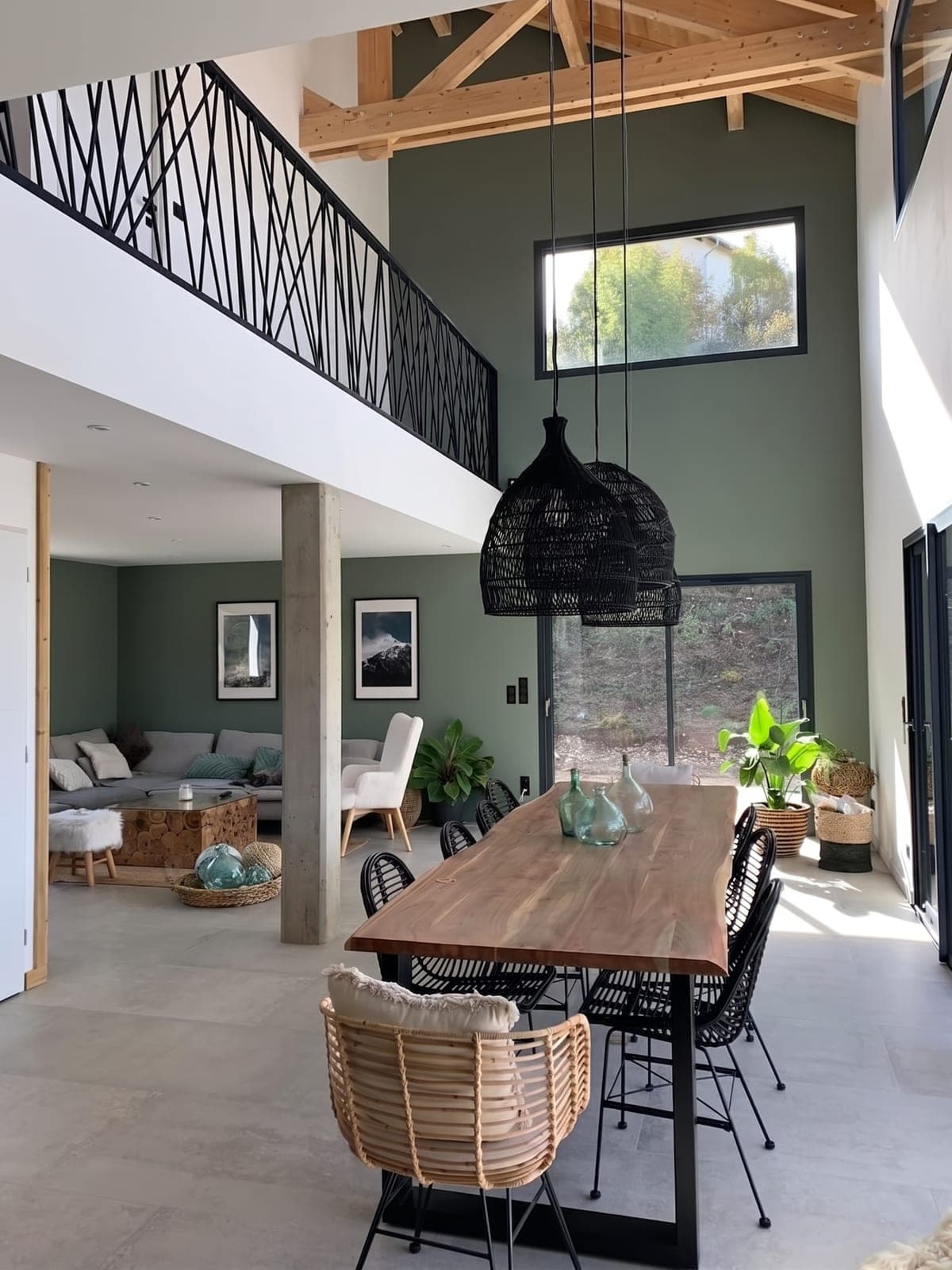 Grande pièce de vie sous mezzanine : charpente apparente, longue table en bois pour huit et salon en contrebas